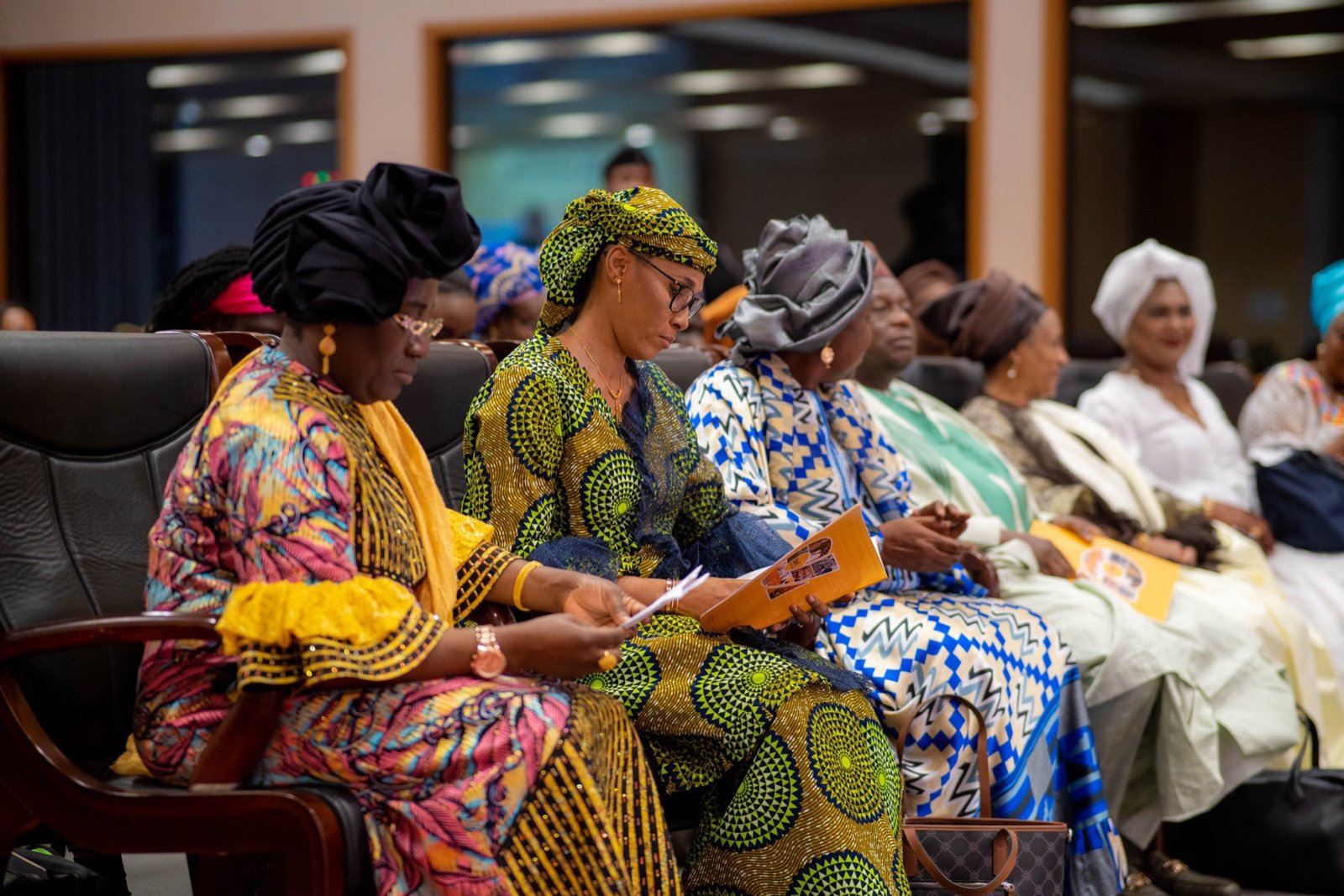 Women in colorful traditional headwraps seated together at a community seminar