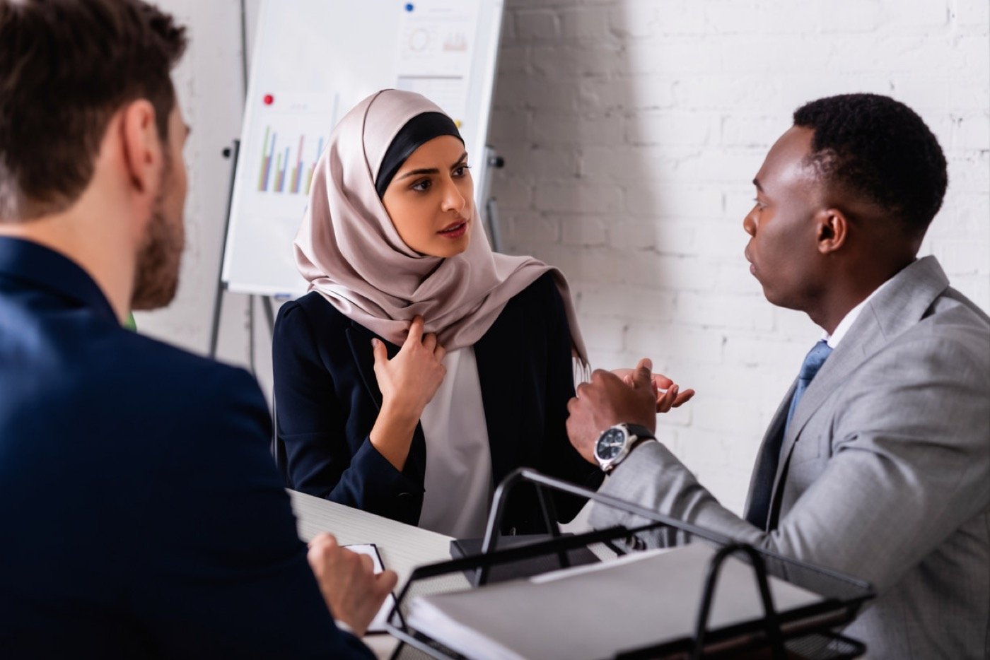 Three colleagues, including a woman wearing a hijab, in an intent discussion during an office meeting
