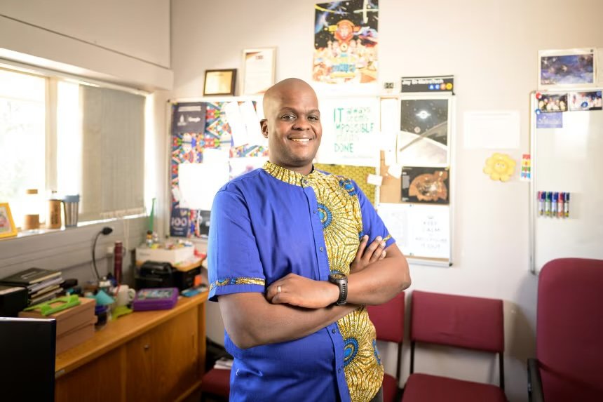 An educator standing confidently in his office, surrounded by classroom materials